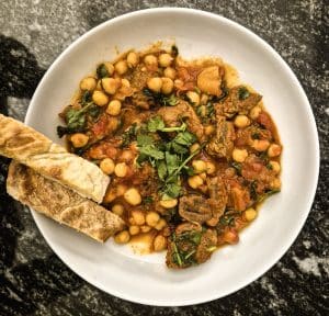 Harissa lamb with chickpeas, tomatoes and dried apricots served in a rustic casserole dish, garnished with fresh herbs
